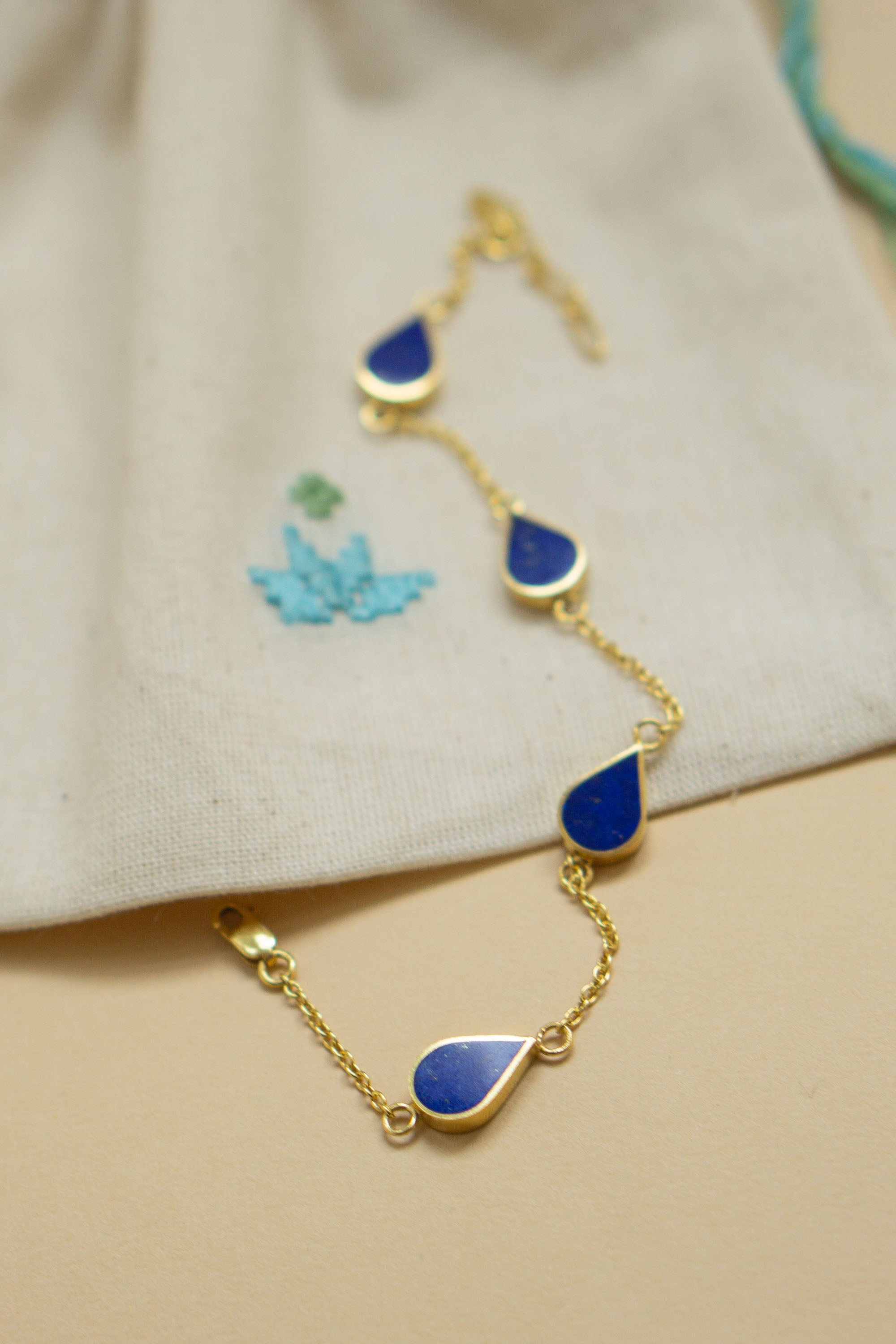 Håndlavet guldarmbånd i 24 karat forgyldt sølv med dråbeformede lapis lazuli sten. En del af Chashma serien, inspireret af Farsis ord for kilde og livets fornyelse. Leveres i en broderet smykkepose skabt af afghanske kvinder.
