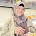 Ayah fra Syrien smilende med en kurv fyldt med håndlavede hæklede produkter, skabt i et kvindekollektiv i Tyrkiet, der fokuserer på inklusivitet og traditionelt håndværk.