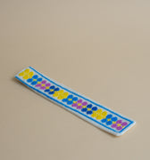 Håndbroderet bogmærke med gule, blå og lilla blomster på en hvid baggrund. Skabt i frihånd af kvinder fra Shatila lejren i Beirut, hvor hvert design er unikt.