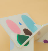 Hvid håndlavet bogholder fremstillet af genanvendt plastik med farverige detaljer i pastelfarver. Skabt af Sasha i Anumo Plastic Studio i Kyiv, med fokus på bæredygtighed og funktionelt design.