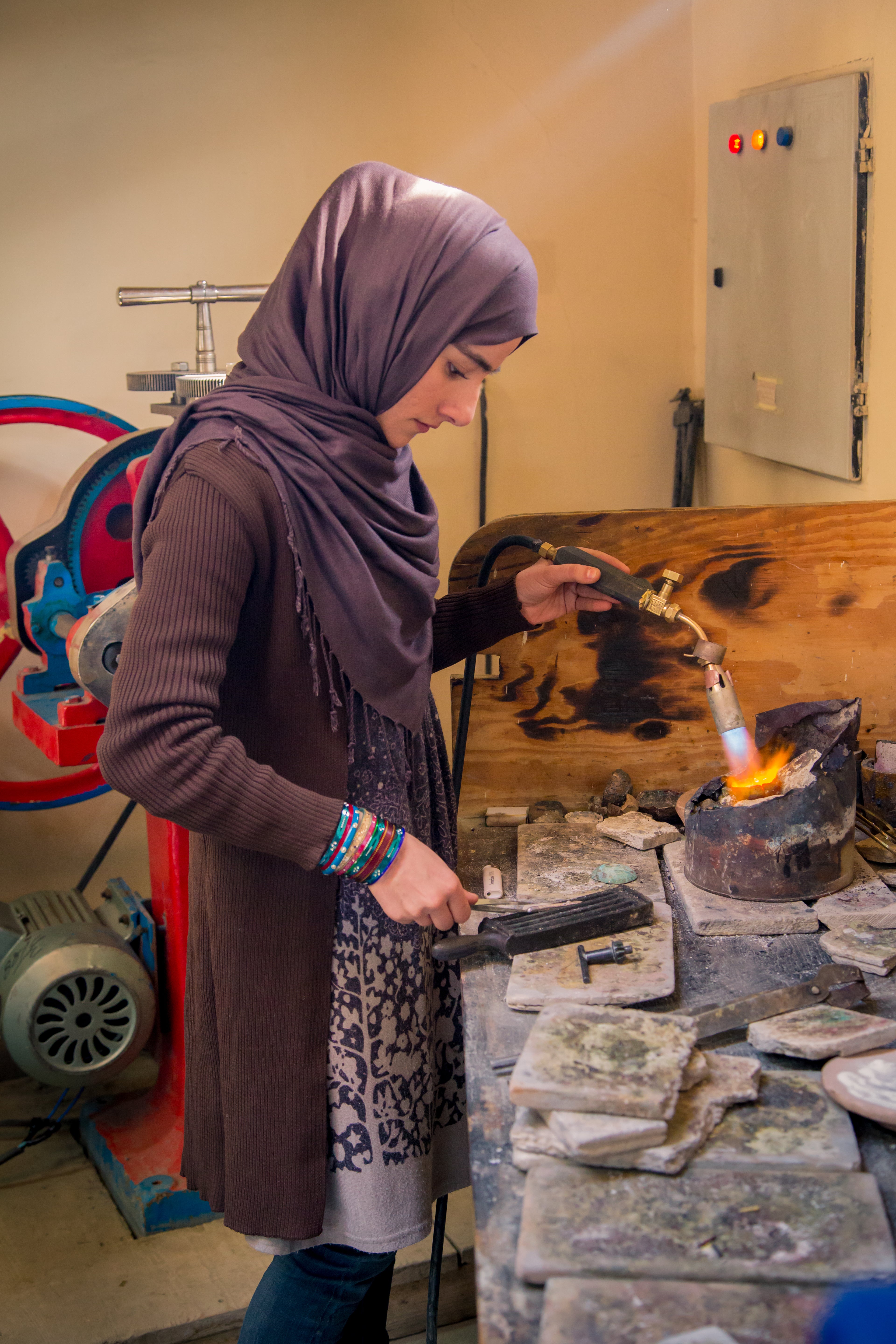 Kvinde i Afghanistan arbejder med smykkefremstilling ved hjælp af flamme og værktøj.