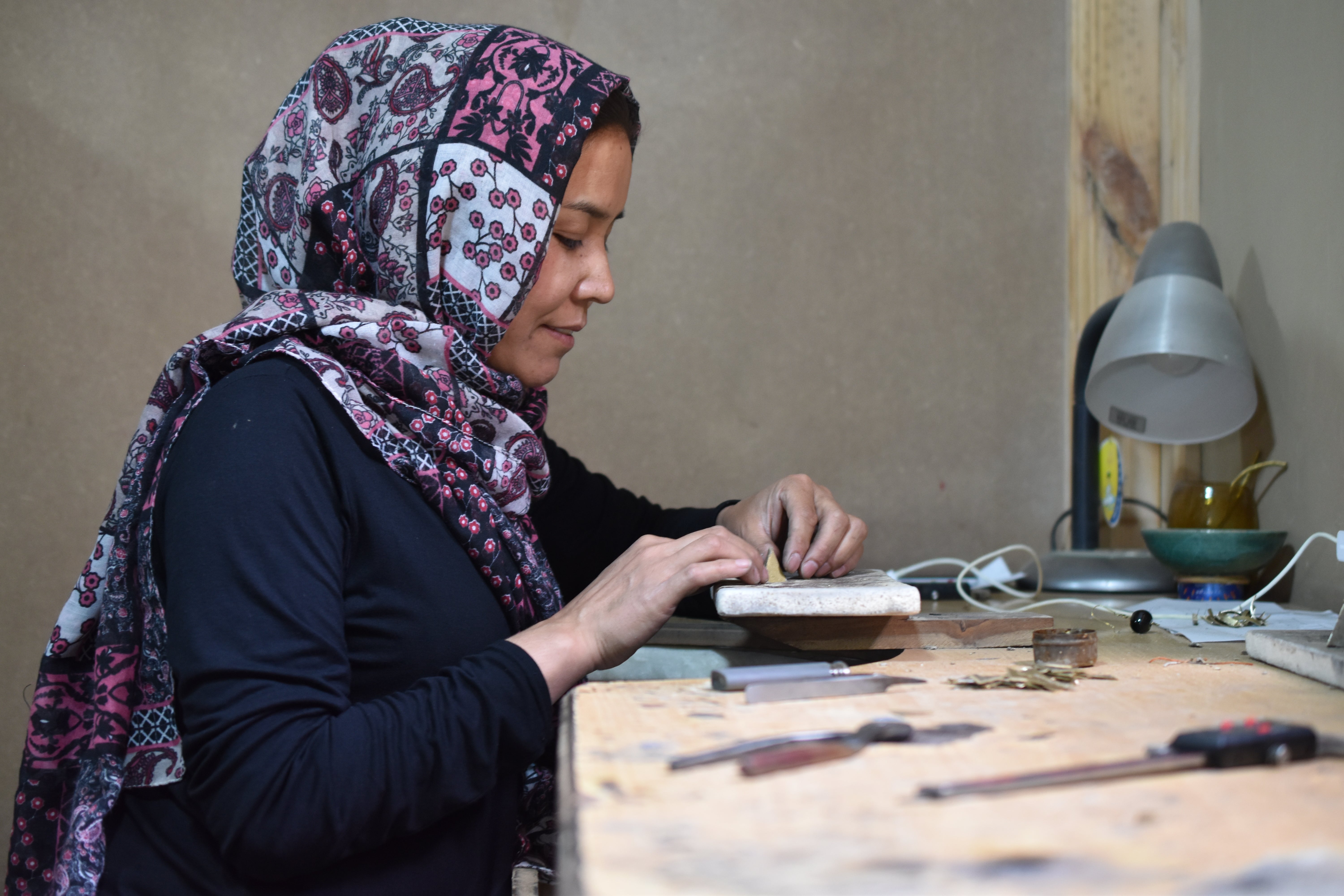 Kvinde fra Afghanistan arbejder på smykker i hånden ved en arbejdsstation.