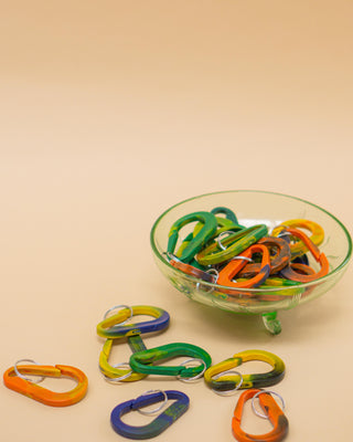 Nøgleringe lavet af genanvendt plastik i forskellige farver ligger i en skål og spredt omkring.