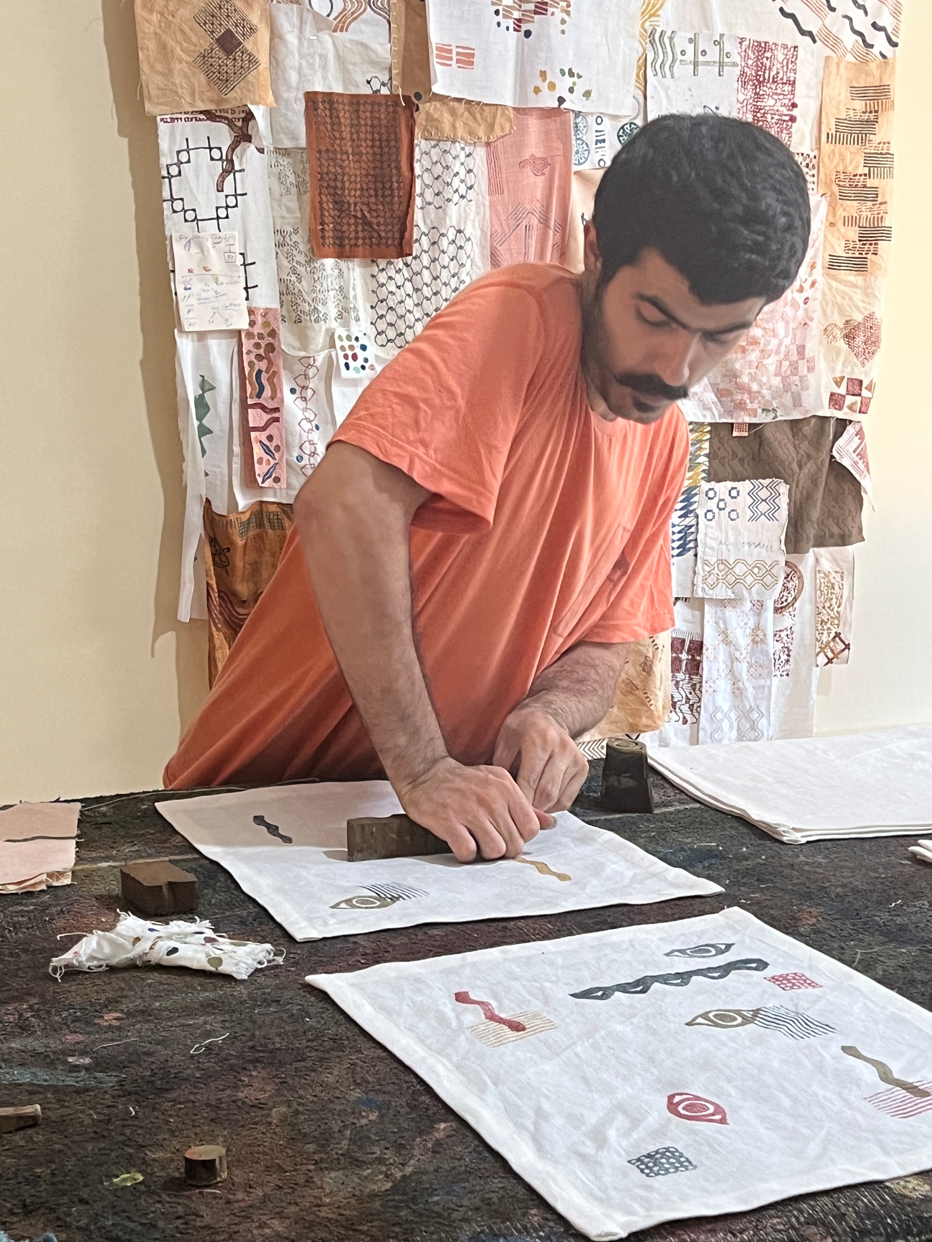 Shadi håndtrykker en dækkeserviet i 100% rest-hør med traditionelle syriske blokprint i sit designstudie i Beirut. De detaljerede mønstre trykkes med hundredårige træstempler fra Damascus, som han og hans bror har hentet. Bag ham hænger tidligere designs og eksperimenter med blokprint.